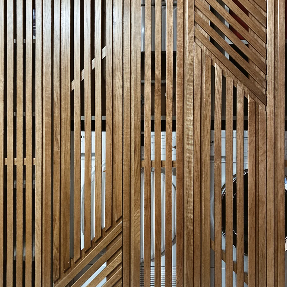 Nahaufnahme einer Front aus vertikalen Eichenlamellen in geometrischem Muster, hinter dem Glas sind Umrisse von Geräten zu erkennen