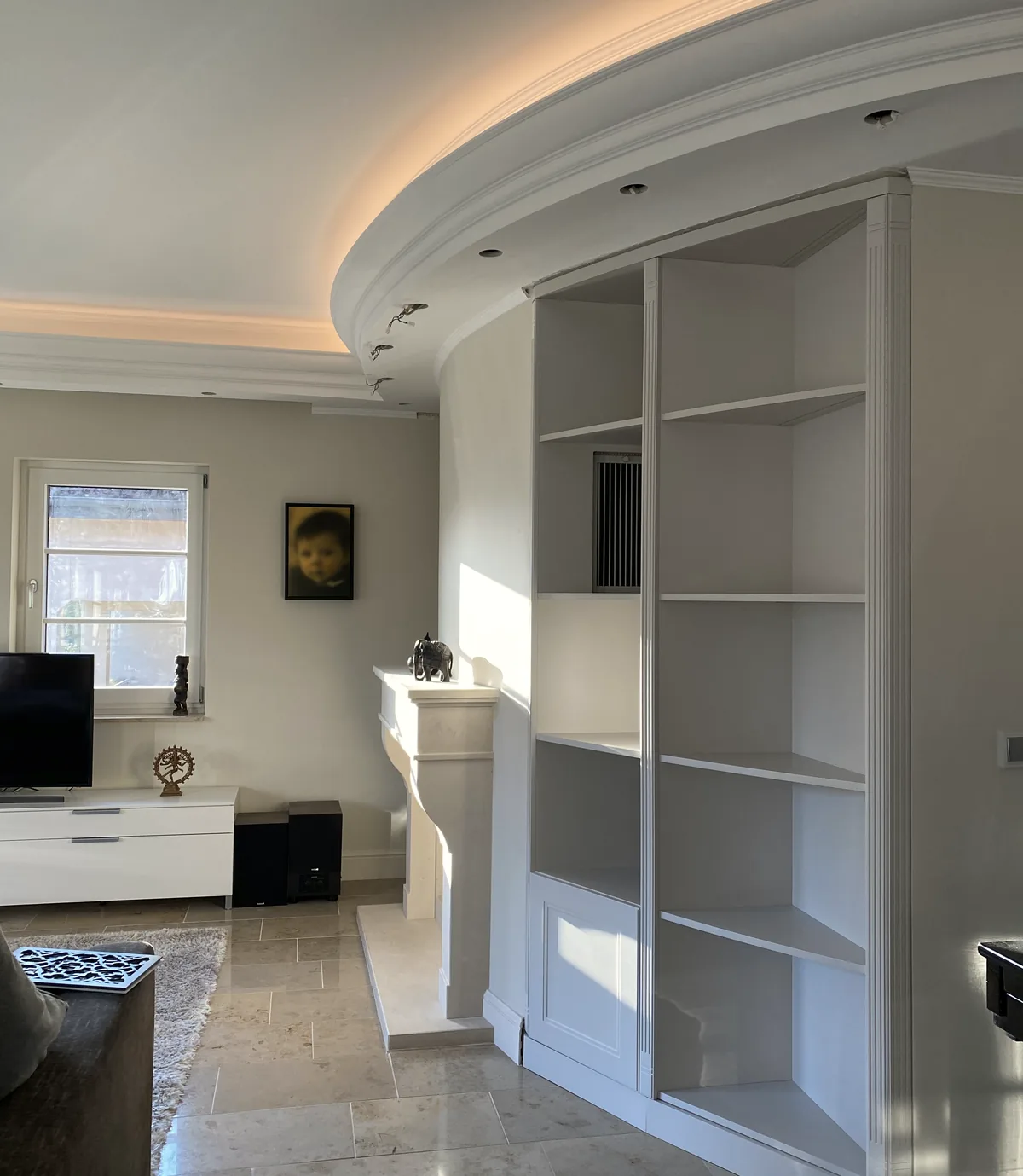 Eckschrank mit Regalen unter der runden Decke, im Vordergrund ein kleiner Teppich und ein dunkler Tisch