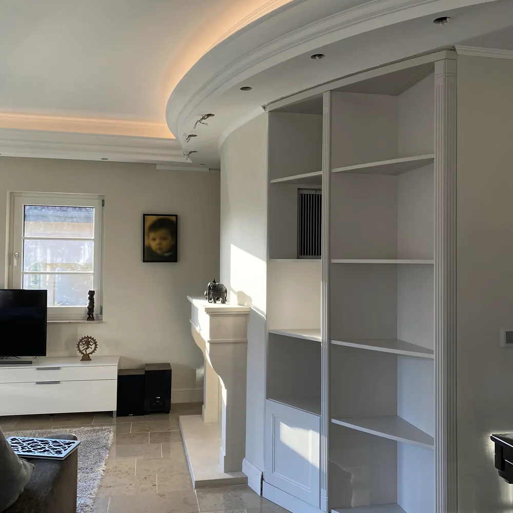 Eckschrank mit Regalen unter der runden Decke, im Vordergrund ein kleiner Teppich und ein dunkler Tisch